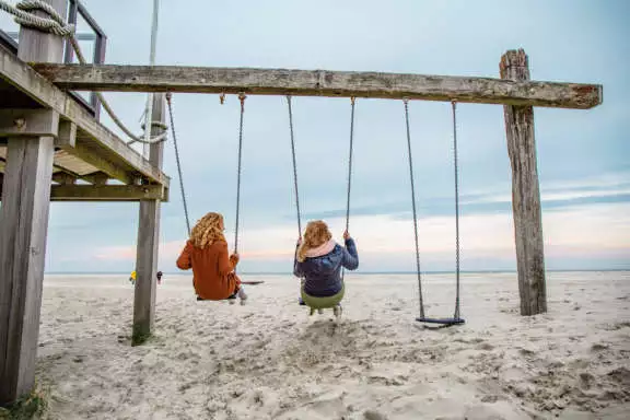 twee vrouwen schommelen op het strand van Terschelling West aan Zee Noordzee op achtergrond