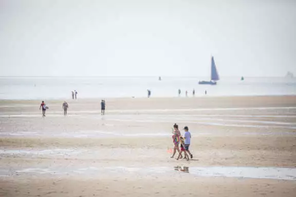 Droogliggers schepen die bij eb blijven steken in het strandzand met wandelaars op de voorgrond nabij West-Terschelling