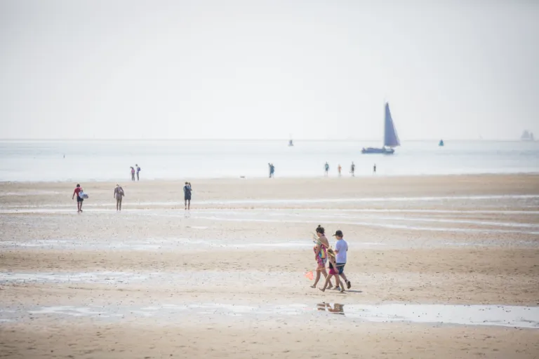 Droogliggers schepen die bij eb blijven steken in het strandzand met wandelaars op de voorgrond nabij West-Terschelling